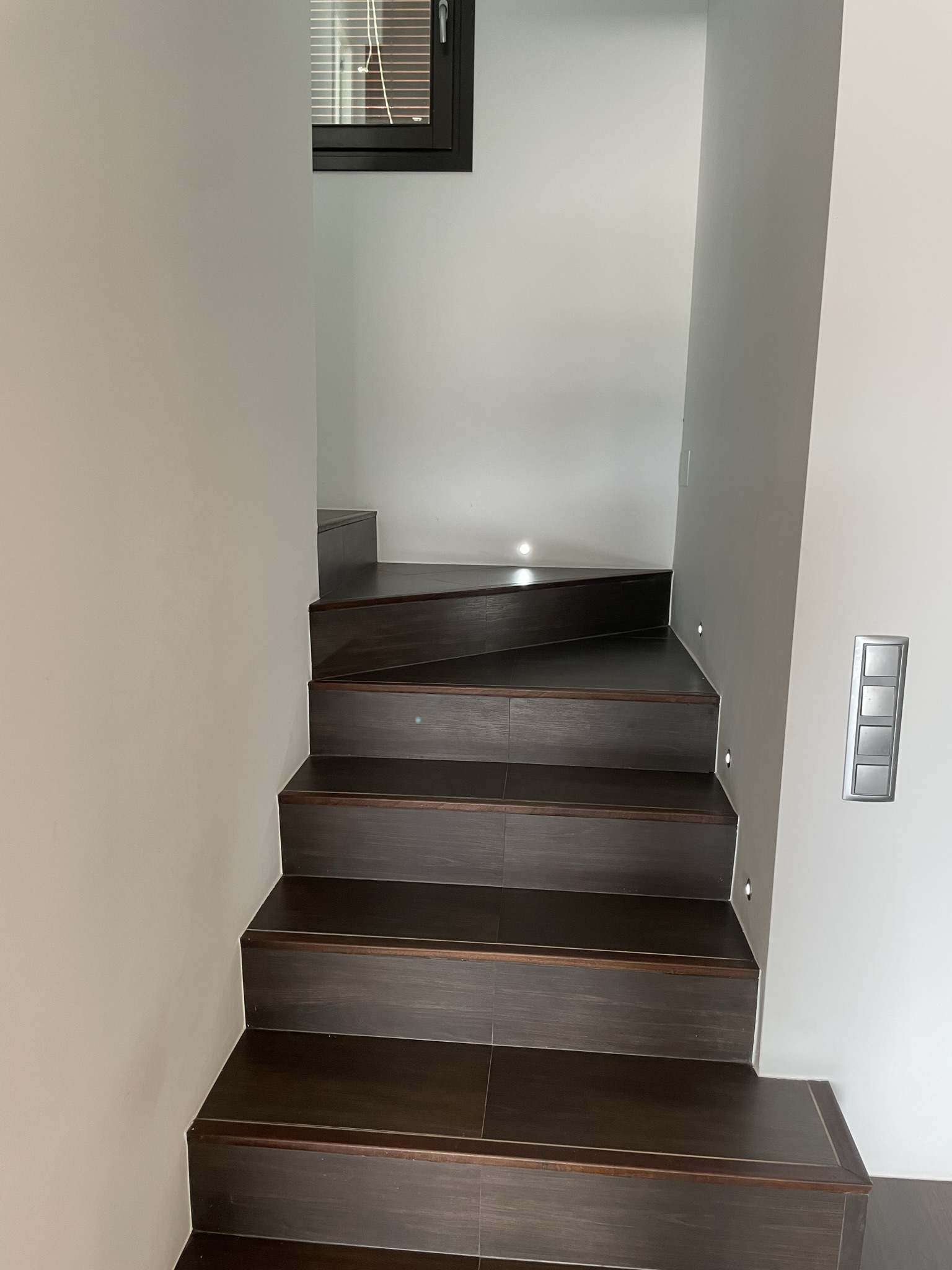 Interne trap met donkere houtlook treden, geïntegreerde LED-wandverlichting en een strakke, moderne afwerking die naar de bovenverdieping leidt.