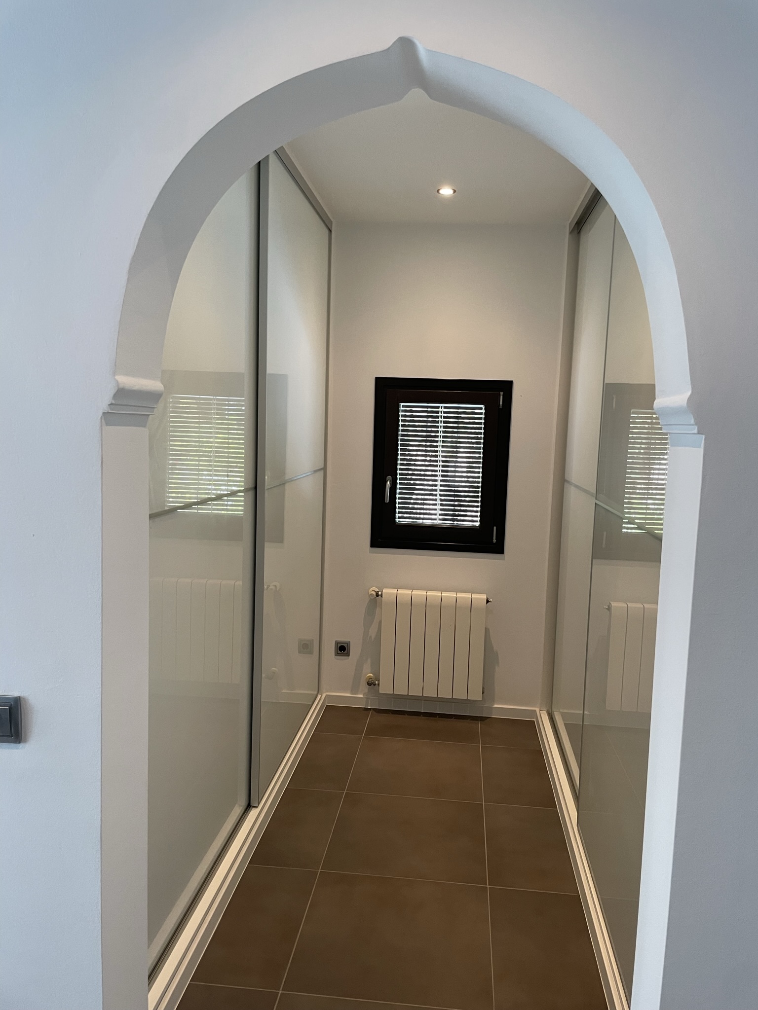 Kleedruimte met kamerhoge inbouwkasten met schuifdeuren, bereikbaar via een karakteristieke boog en voorzien van centrale verwarming en inbouwverlichting.