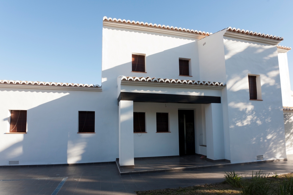 Mediterrane gevel met witte muren, aluminium kozijnen met houtnerf en een traditioneel pannendak boven een schaduwrijke entree met donkere balken.