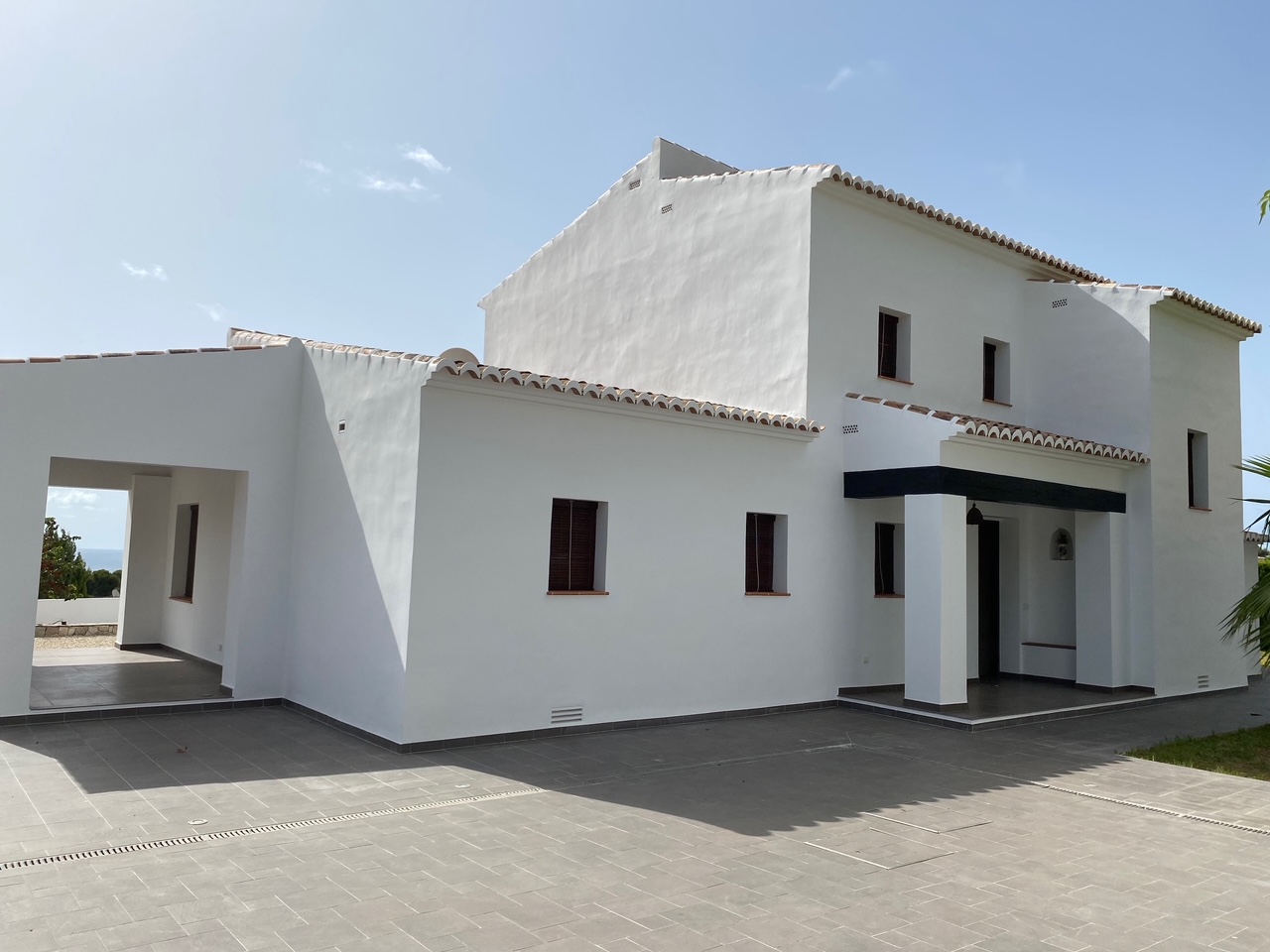 Mediterrane gevel met witte muren, terracotta dakpannen en een groot grijs betegeld terras voorzien van geïntegreerde afwateringsgoten.