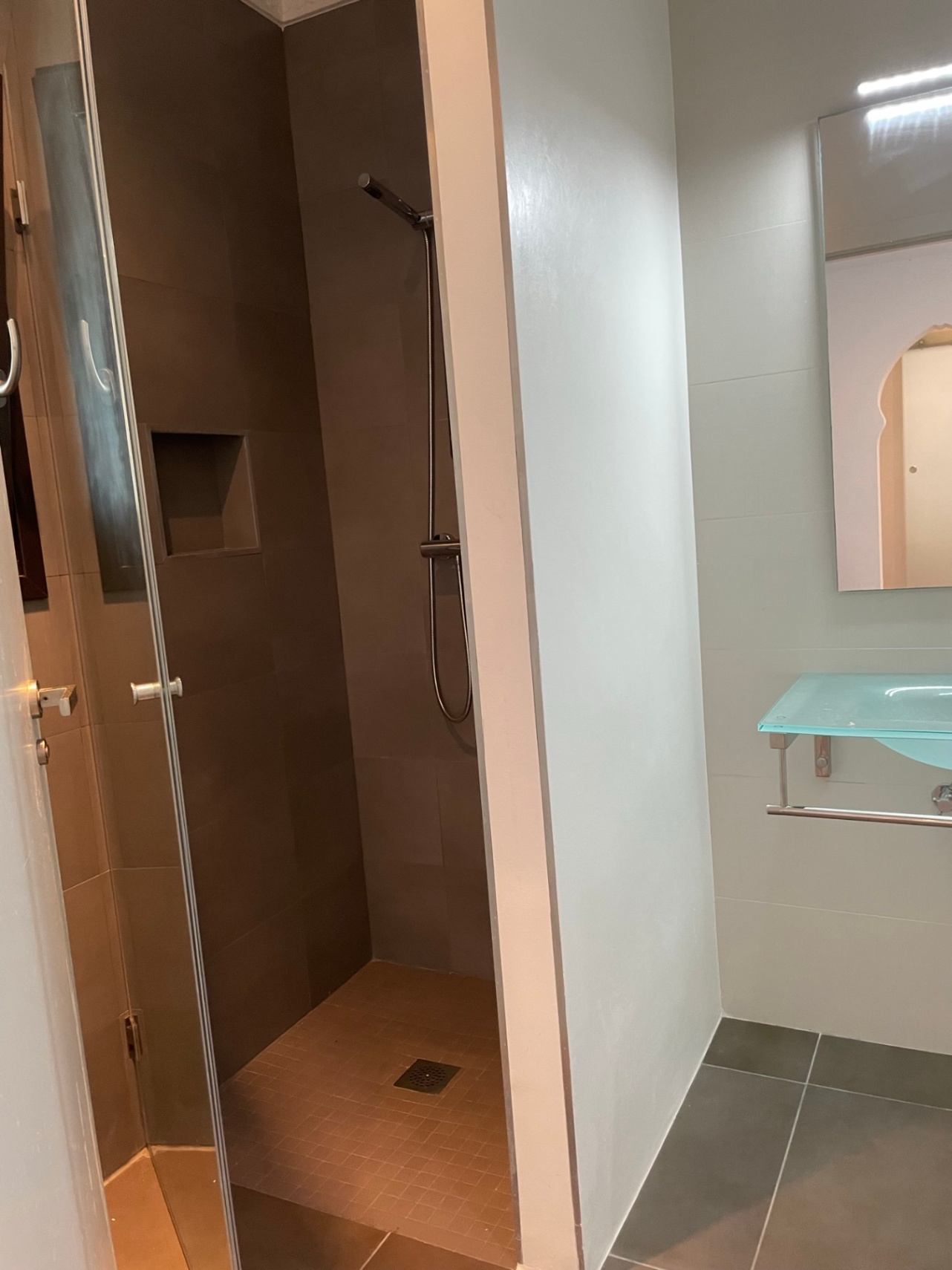 Moderne badkamer met inloopdouche in aardetinten, een ingebouwde nis en een stijlvolle glazen wastafel.