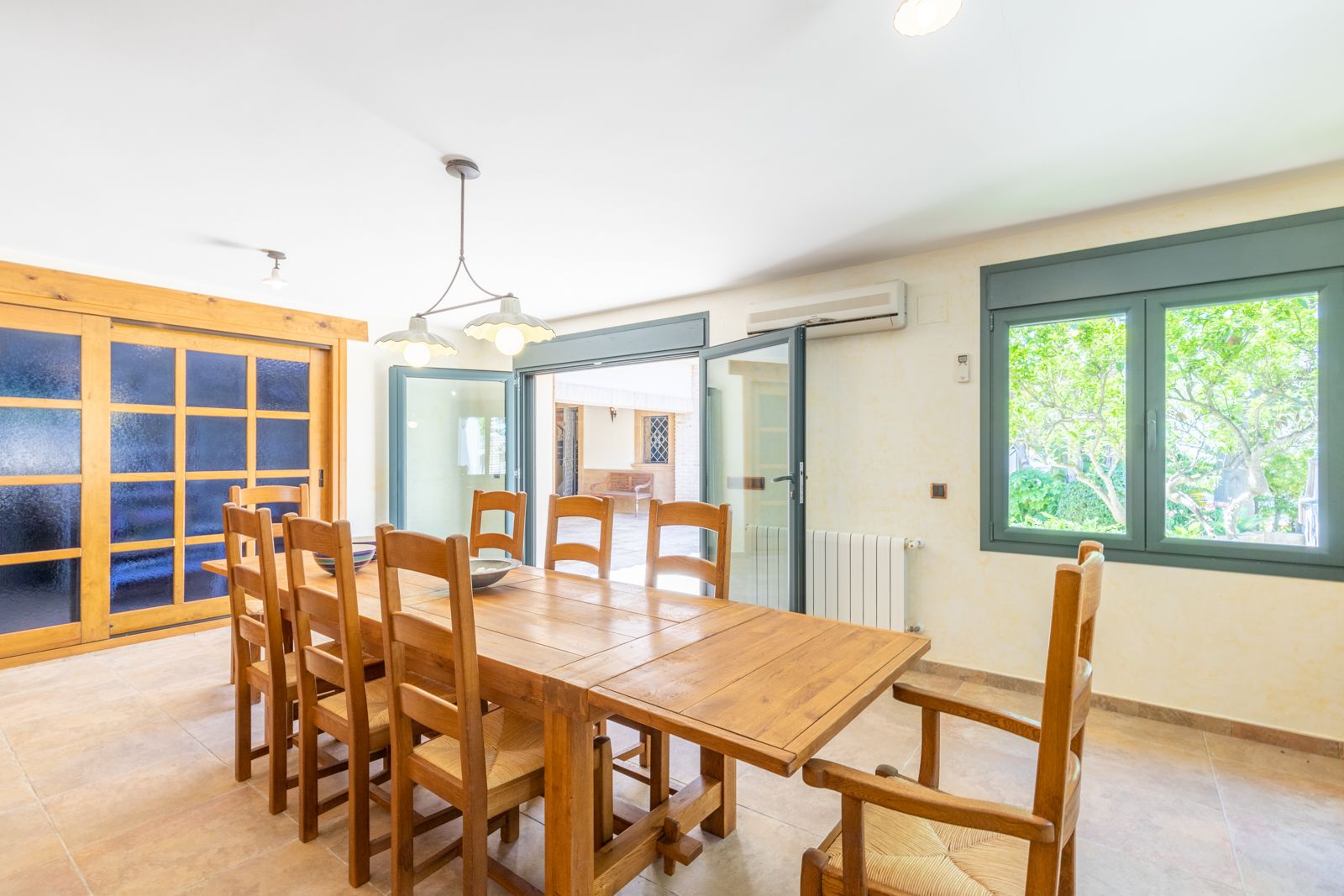 Lichte eetkamer met massief houten tafel en bijpassende stoelen, toegang tot terras en raam met uitzicht op de tuin.
