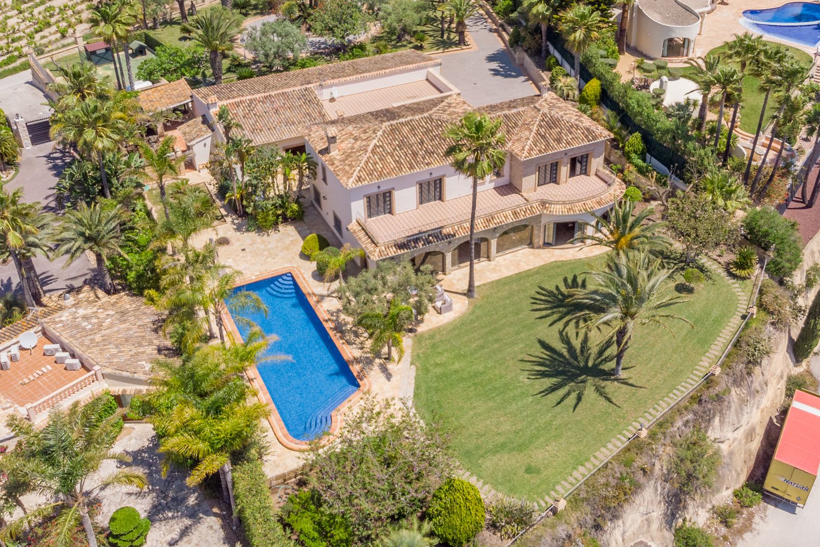 Luchtfoto van het landgoed met blauw zwembad, volgroeide tuinen en mediterrane architectuur.
