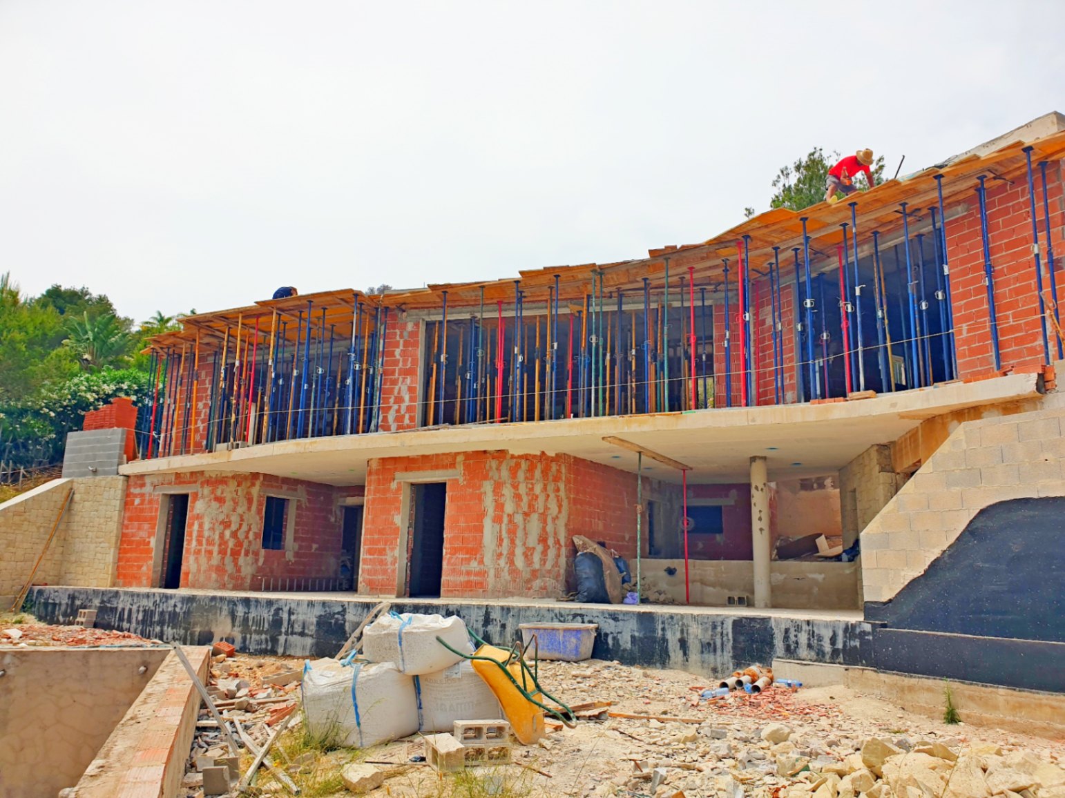 Buitenaanzicht van de villa in de ruwbouwfase, met de bakstenen structuur, betonnen vloeren en de kenmerkende gebogen lijnen van de bovenverdieping.