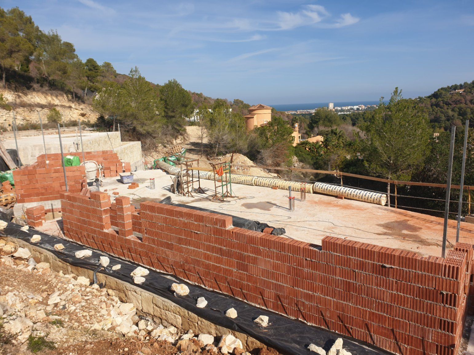 Huidige bouwfase met de eerste keramische bakstenen muren op de fundering, met een panoramisch uitzicht over de Middellandse Zee en de kust van Jávea.