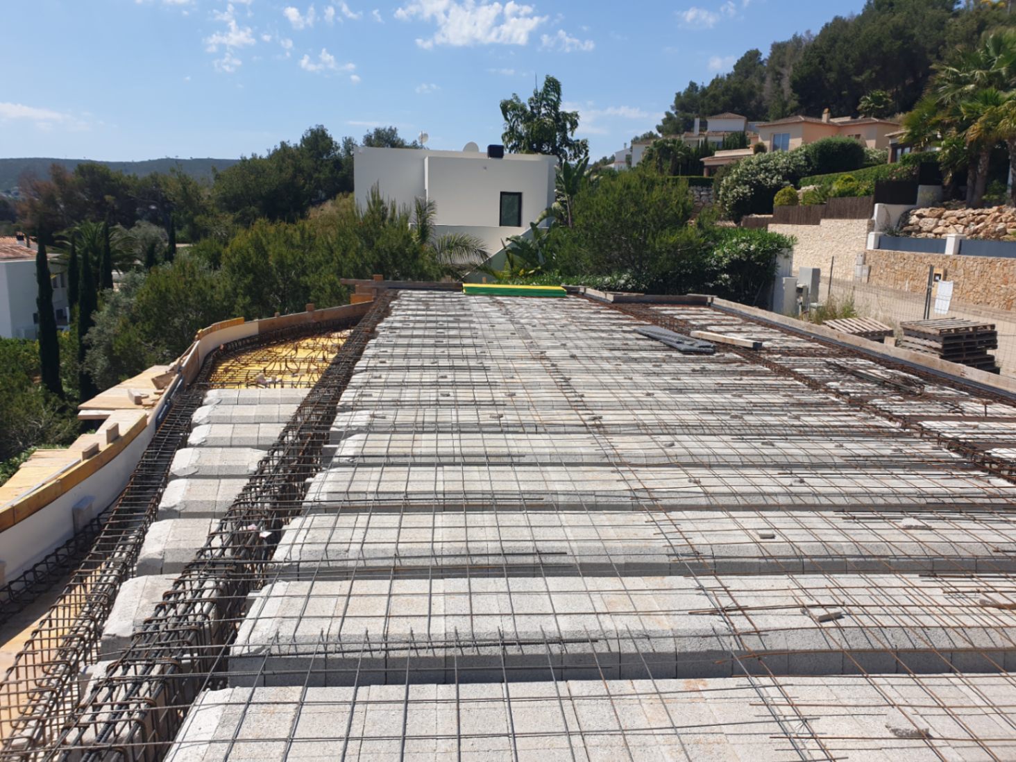 Huidige bouwfase van de vloerplaat met betonblokken en staalvlechtwerk op een verhoogd perceel in Jávea met uitzicht op de omgeving.