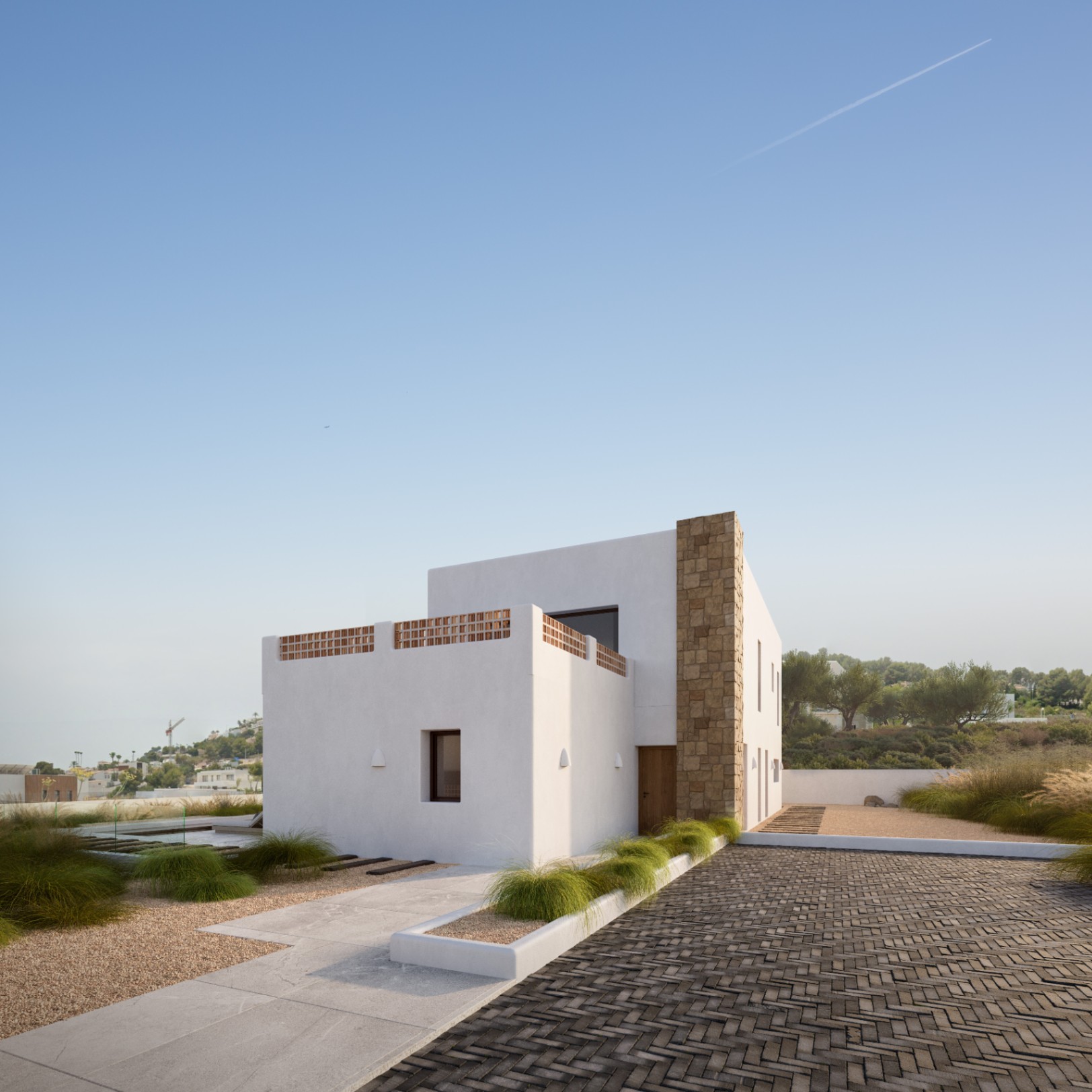 Moderne mediterrane gevel met witte muren, een natuurstenen kolom en terras met terracotta vlechtwerk, omgeven door een minimalistische tuin met bestrate paden.