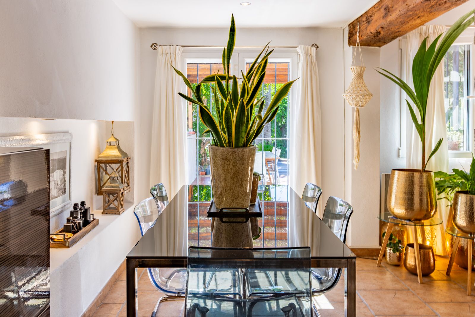 Lichte eetkamer met glazen tafel, transparante stoelen en authentieke houten balken. Openslaande deuren bieden directe toegang tot het terras.