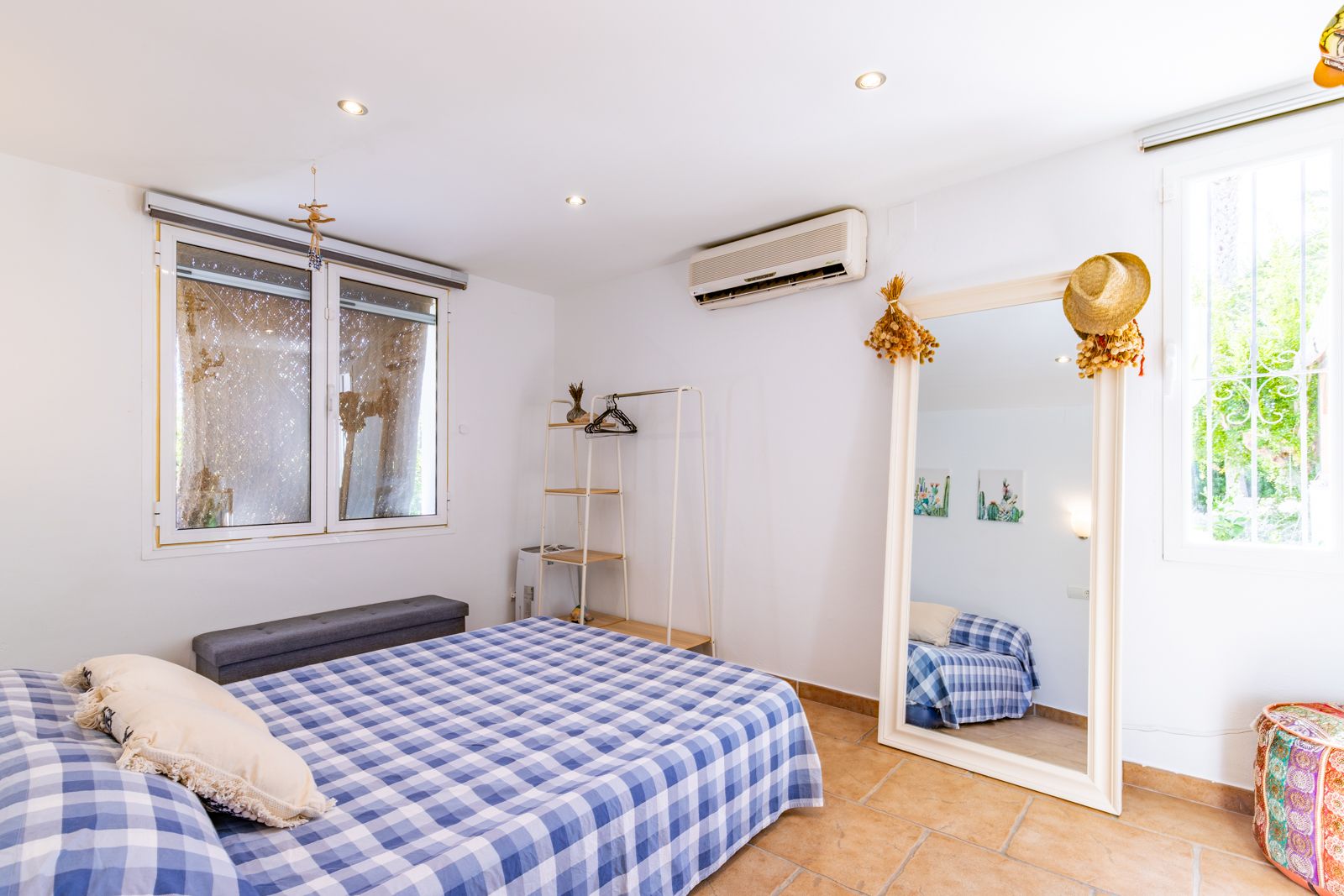 Lichte slaapkamer met terracotta vloertegels, airconditioning en een grote passpiegel. Voorzien van inbouwspots en natuurlijke lichtinval via het venster.