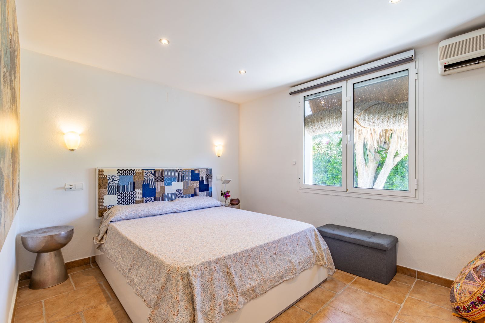 Lichte slaapkamer met terracotta vloertegels, een patchwork hoofdbord, airconditioning en uitzicht op de omliggende tuin.