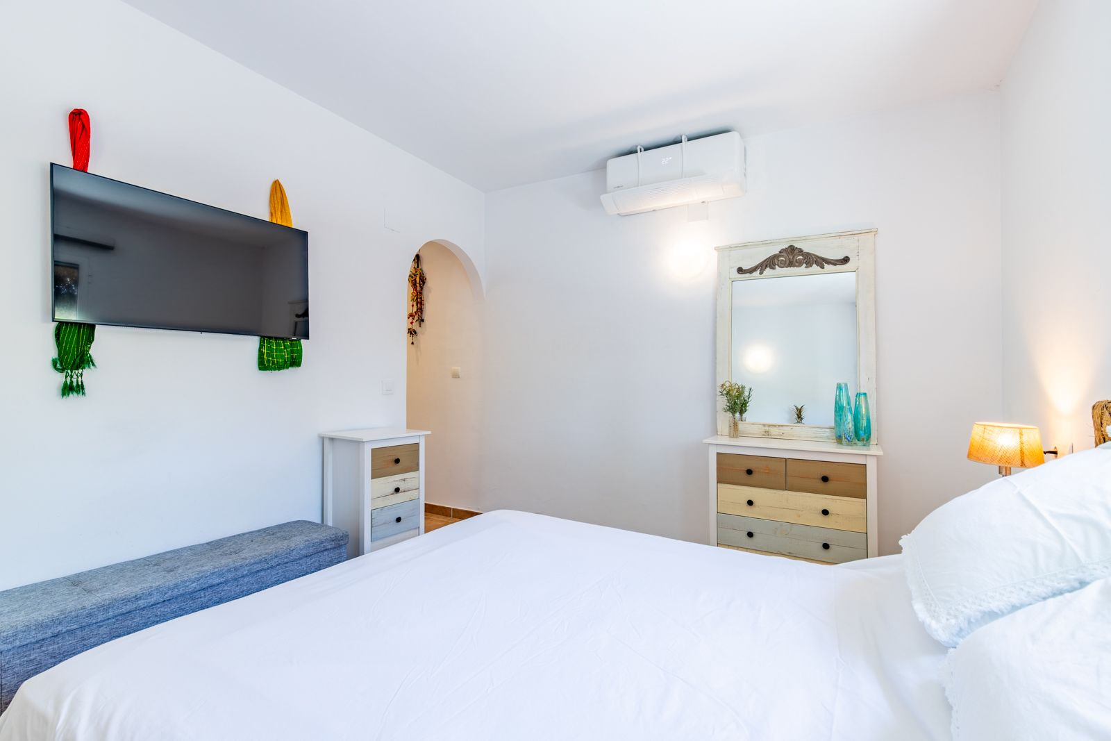 Lichte slaapkamer met tweepersoonsbed, rustieke ladekasten, airconditioning en een aan de muur gemonteerde televisie.