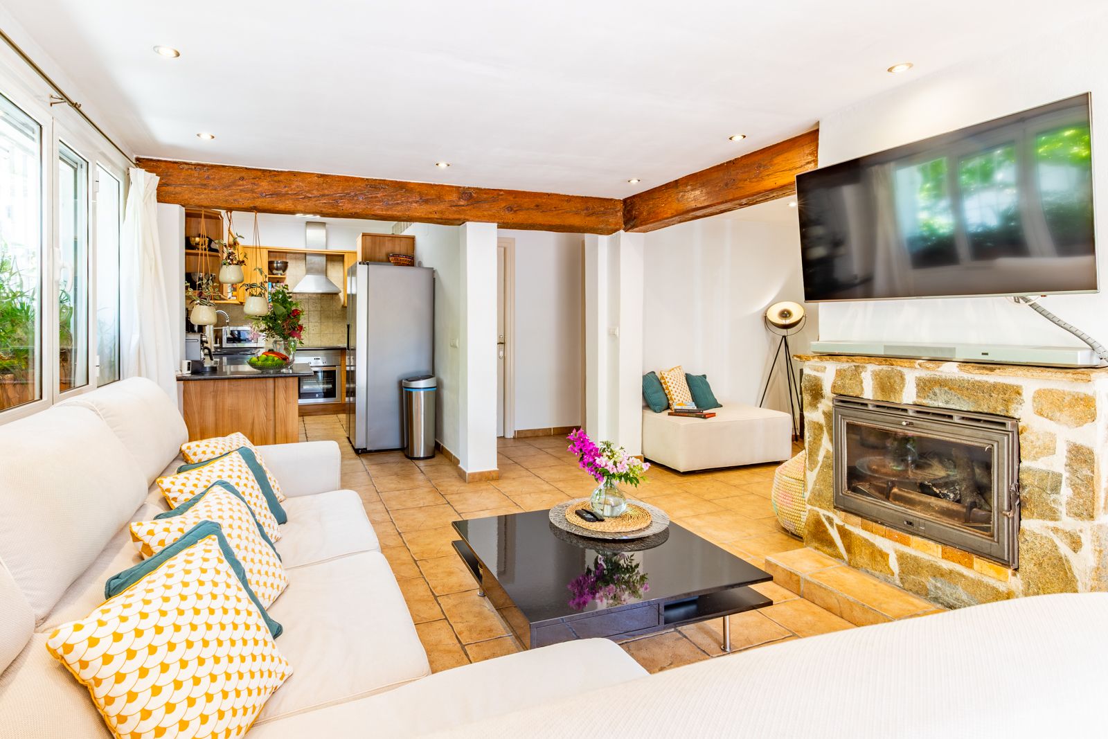Lichte woonkamer met houten balkenplafond, natuurstenen open haard en tegelvloer, in open verbinding met de functionele keuken.