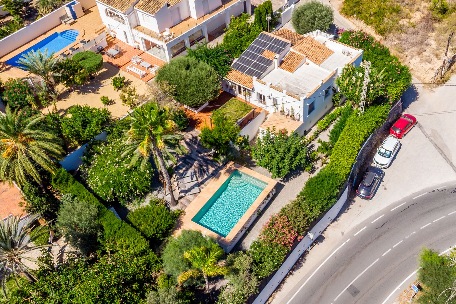 Luchtfoto van de villa met het rechthoekige zwembad, de weelderige mediterrane tuin en de zonnepanelen op het traditionele pannendak.