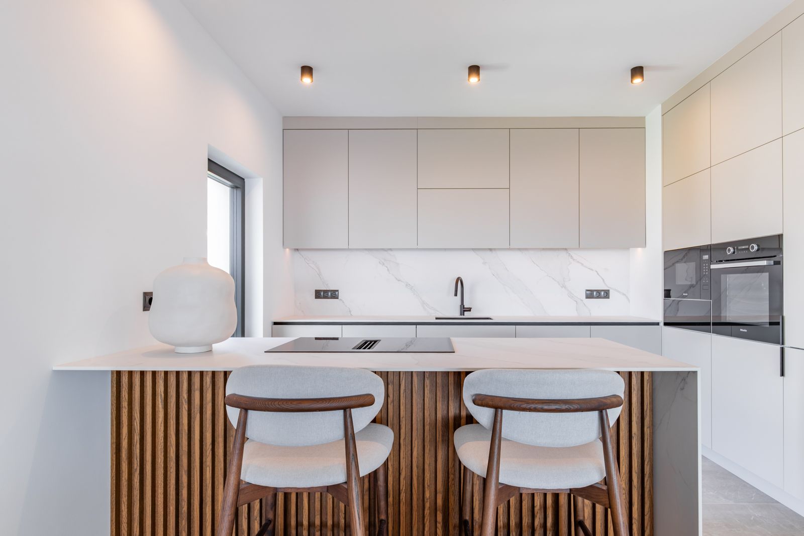 Designkeuken met een kookeiland van eikenhouten latten, werkbladen van gesinterd steen en geïntegreerde Miele-apparatuur in minimalistische kasten.