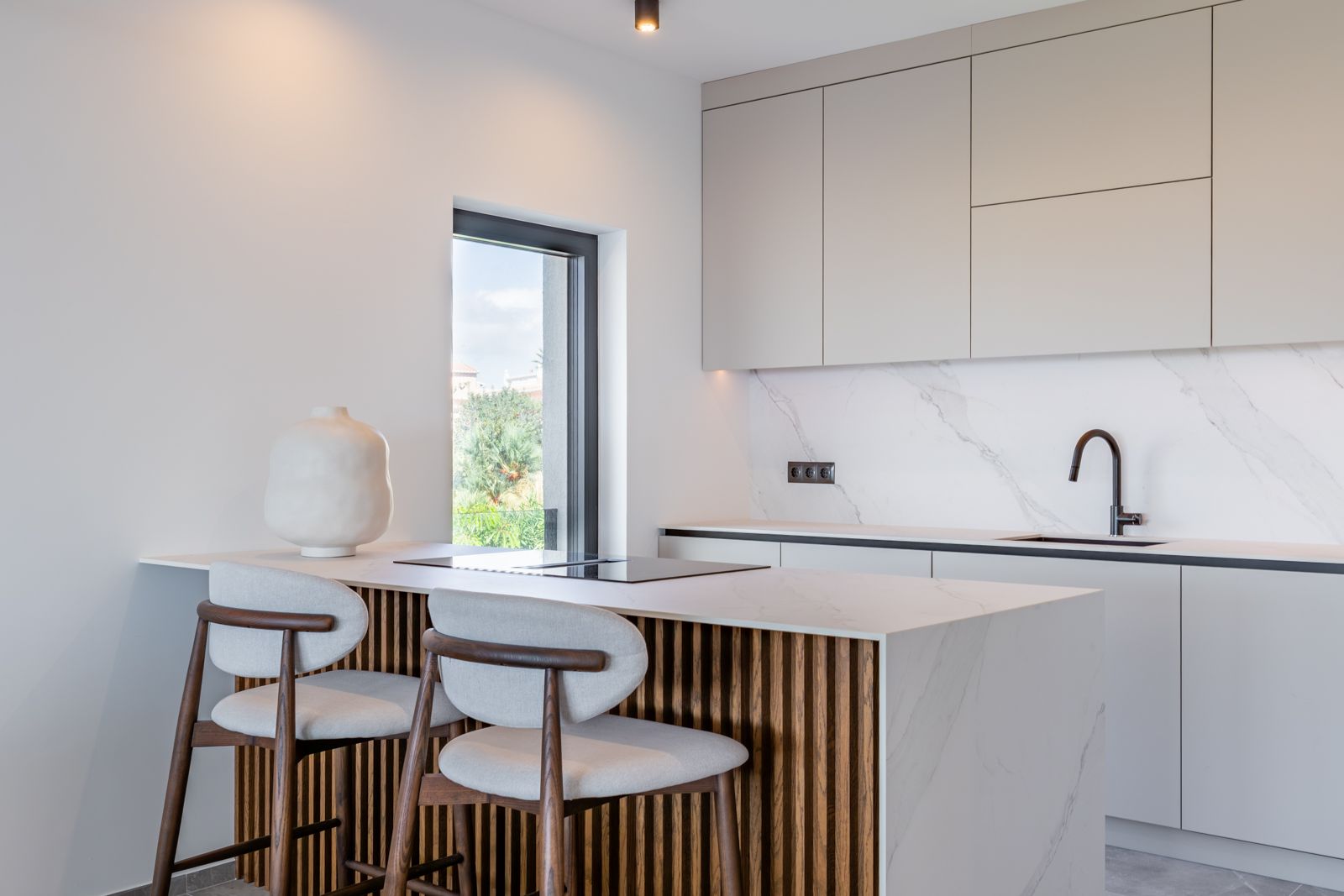 Designkeuken met kookeiland in marmerlook gesinterd steen, afgewerkt met houten latten en voorzien van een geïntegreerde inductiekookplaat en minimalistische zwarte kranen.
