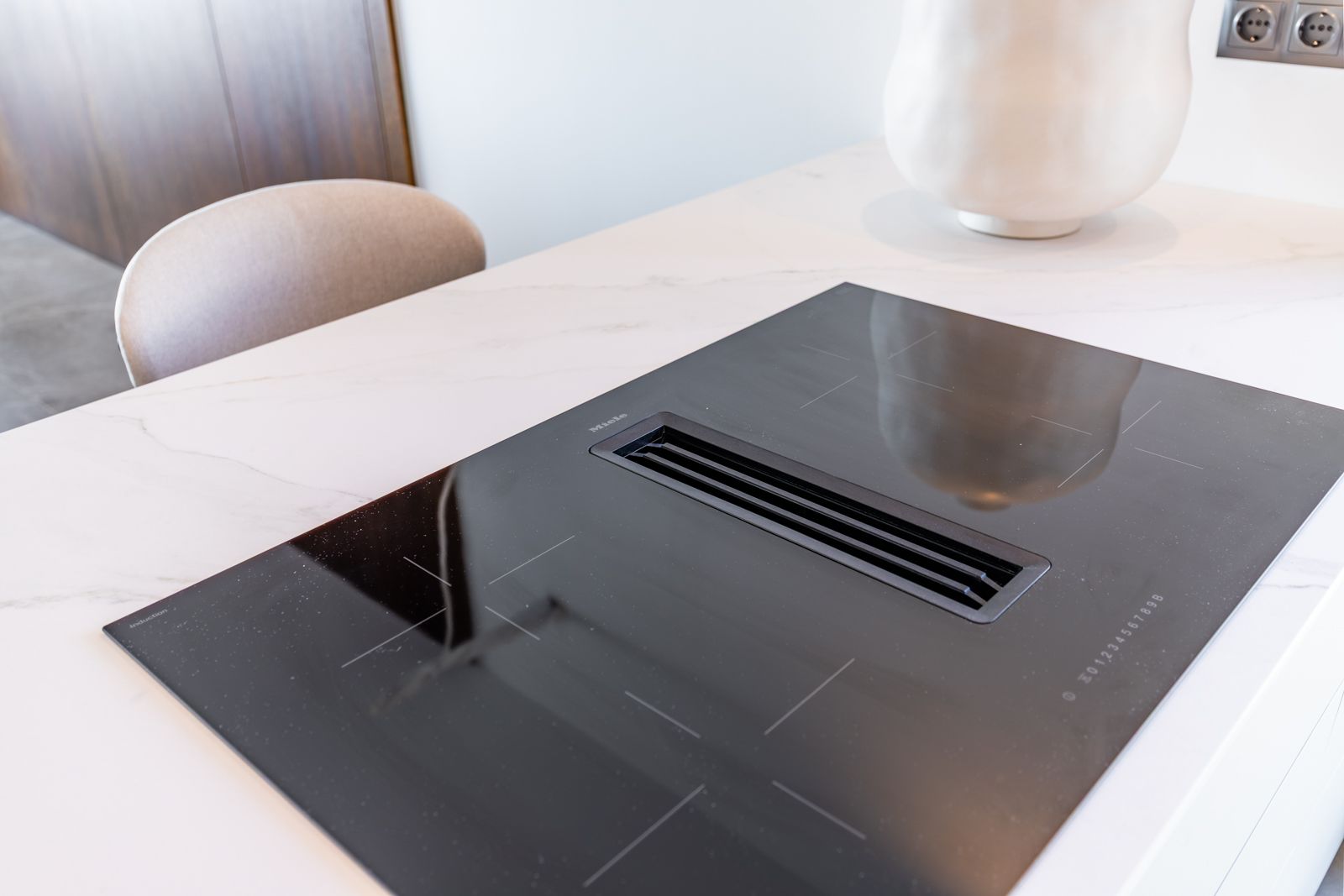 Miele inductiekookplaat met geïntegreerde afzuiging gemonteerd in een wit marmerlook gesinterd stenen werkblad.