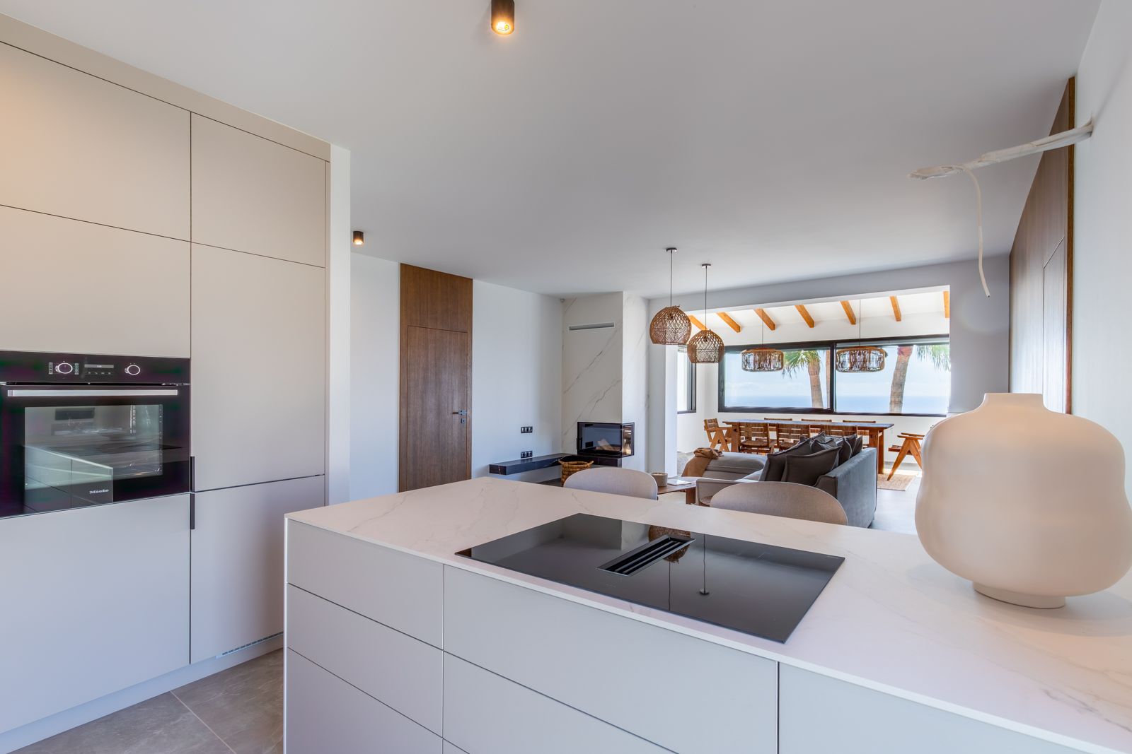 Open designkeuken met kookeiland van gesinterd steen, geïntegreerde inductiekookplaat, Miele-apparatuur en uitzicht op de woonkamer en de Middellandse Zee.