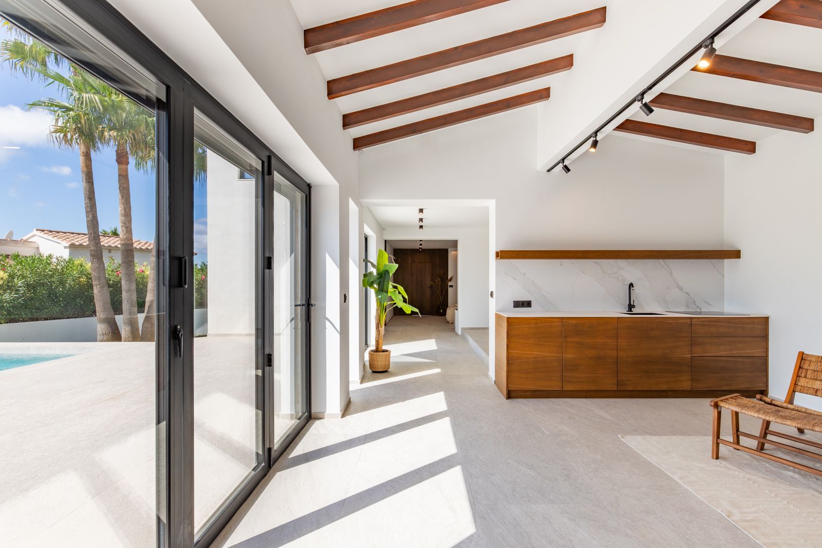 Open woonruimte met zichtbare houten balken, een eikenhouten kitchenette en grote glazen schuifdeuren die binnen en buiten bij het zwembad naadloos verbinden.