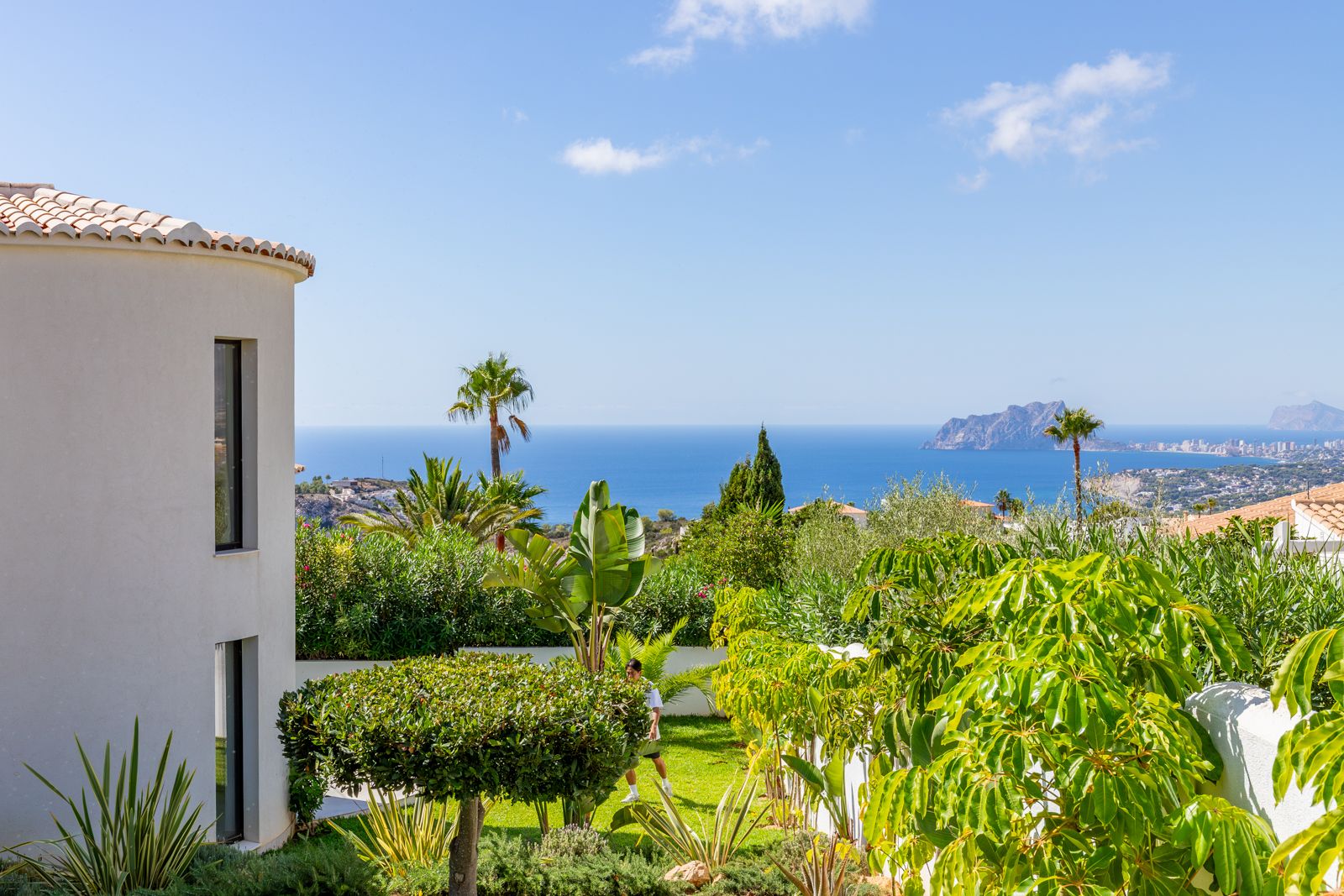 Panoramisch uitzicht op de Middellandse Zee en de Peñón de Ifach vanuit de aangelegde tuin die de moderne, gebogen gevel van de villa omringt.