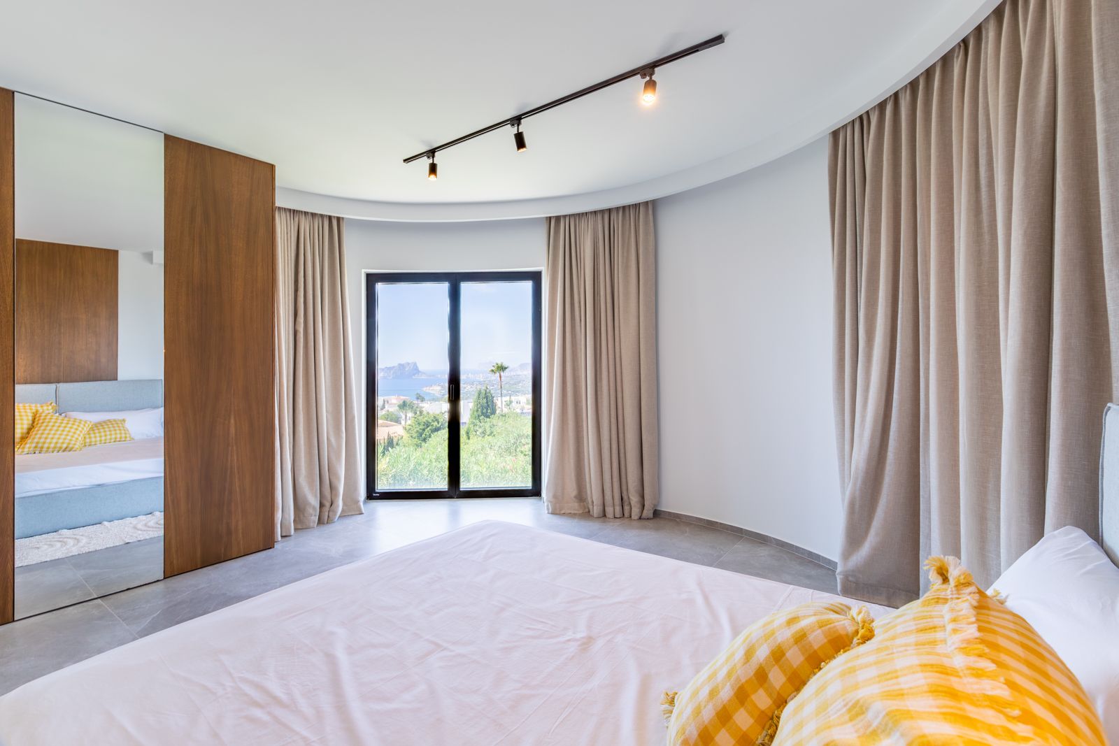 Slaapkamer met een gebogen wand, op maat gemaakte eikenhouten kasten en kamerhoge ramen met uitzicht op de Middellandse Zee en de omliggende natuur.