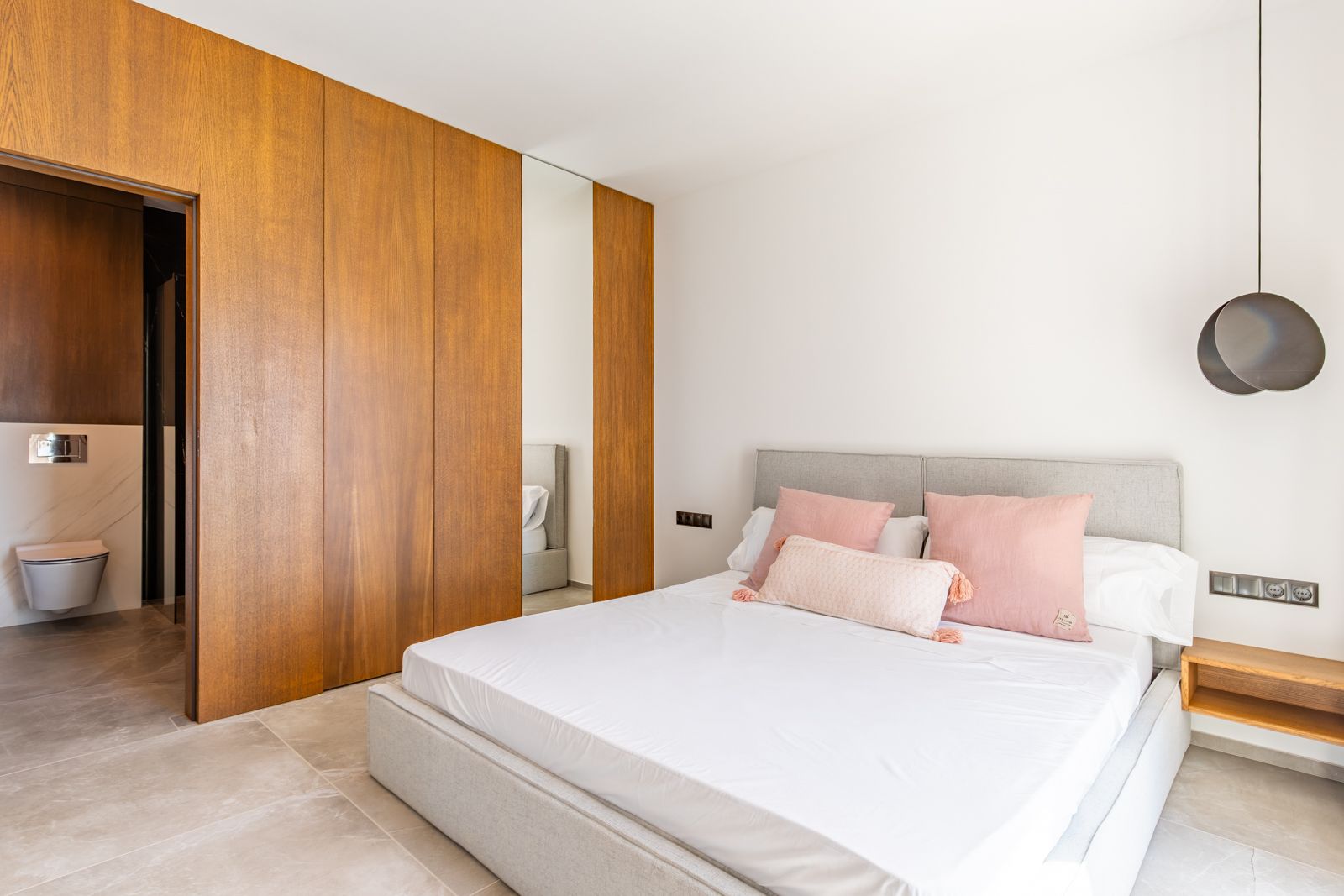 Slaapkamer met maatwerk eikenhouten kasten, grootformaat porseleinen vloeren en een en-suite badkamer met moderne wandcloset en marmerlook.