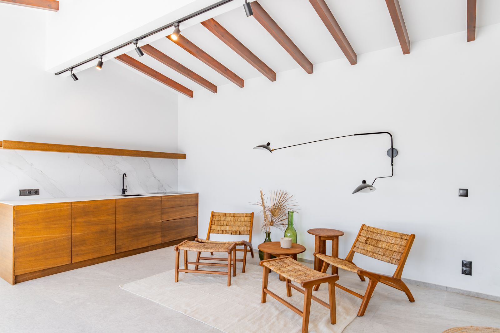 Woonruimte met eiken kitchenette, aanrechtblad van gesinterde steen, houten balken en designstoelen van natuurlijke vezels op een porseleinen vloer.