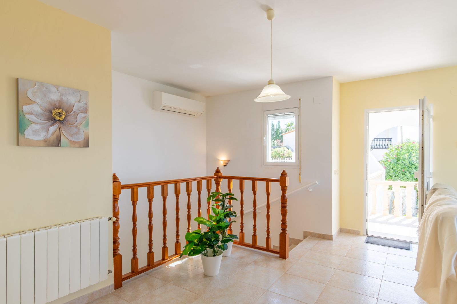 Lichte overloop met keramische tegelvloer, houten balustrade en toegang tot het terras. Voorzien van airconditioning en een radiator voor centrale verwarming.