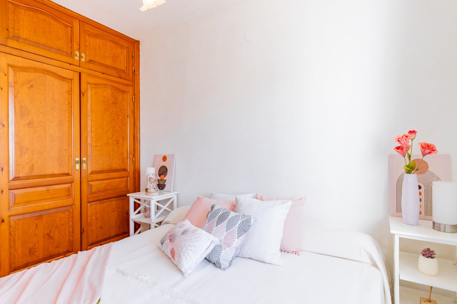 Lichte slaapkamer met een grote ingebouwde houten kast, witte muren en minimalistische nachtkastjes die zorgen voor een rustige en functionele ruimte.
