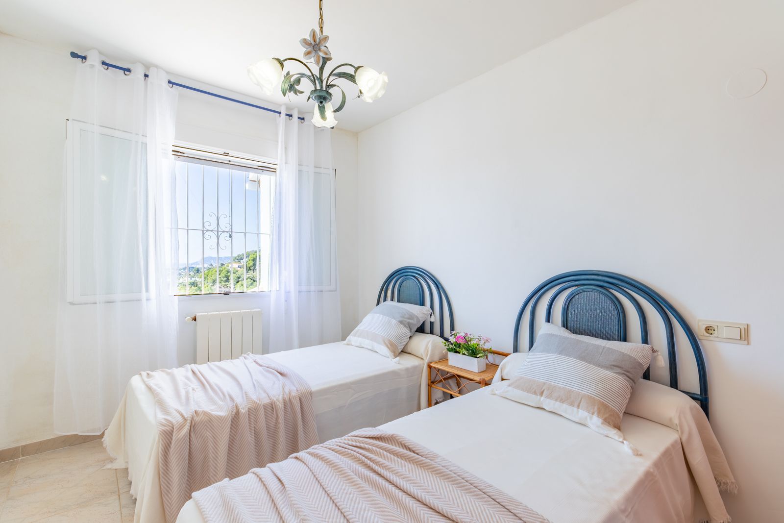 Lichte slaapkamer met twee eenpersoonsbedden, blauwe gebogen hoofdborden, centrale verwarming en raam met uitzicht op de natuurlijke omgeving van Benimeit.