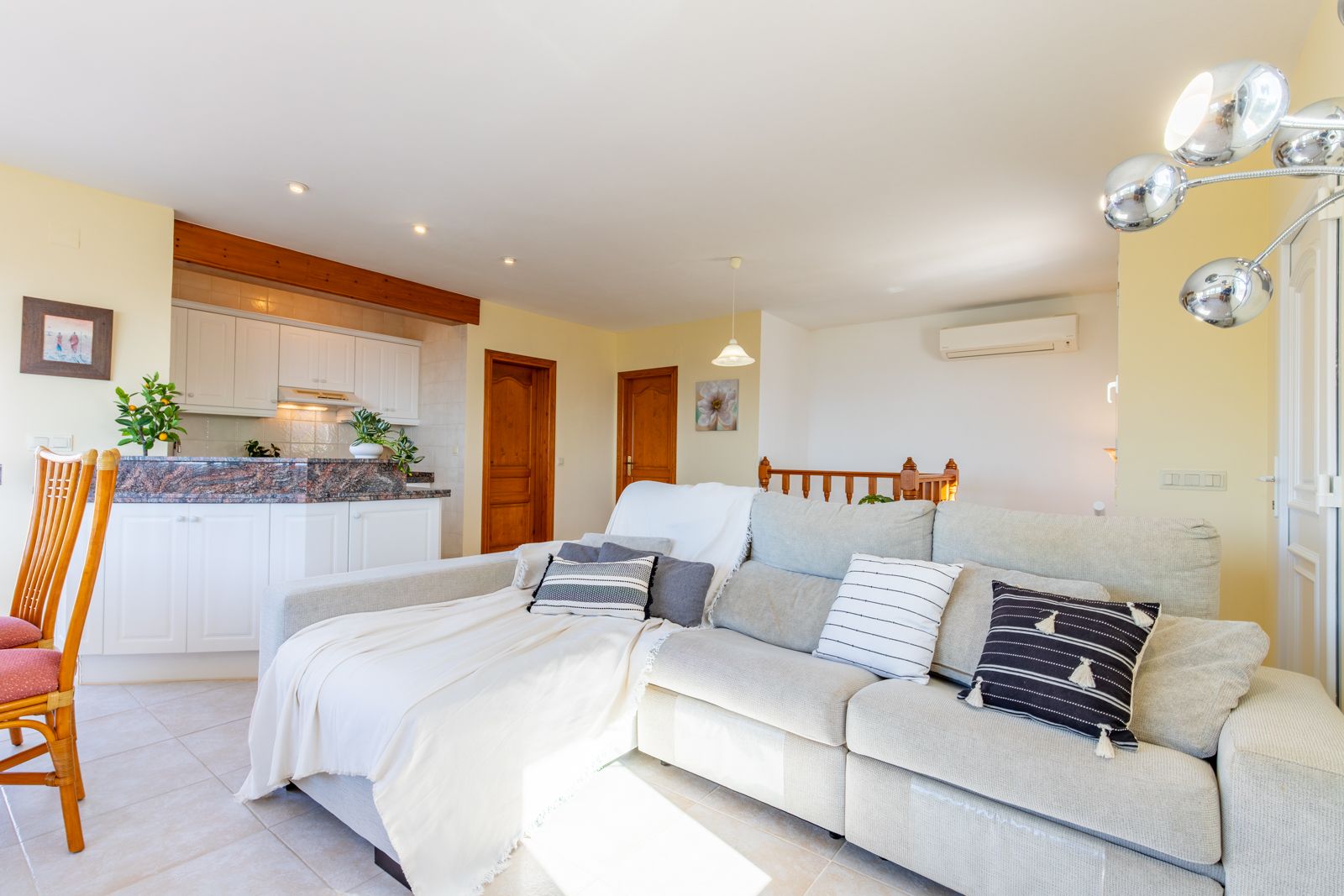 Lichte woonkamer met hoekbank, open keuken voorzien van granieten aanrechtblad, houten balken, airconditioning en een plavuizen vloer.