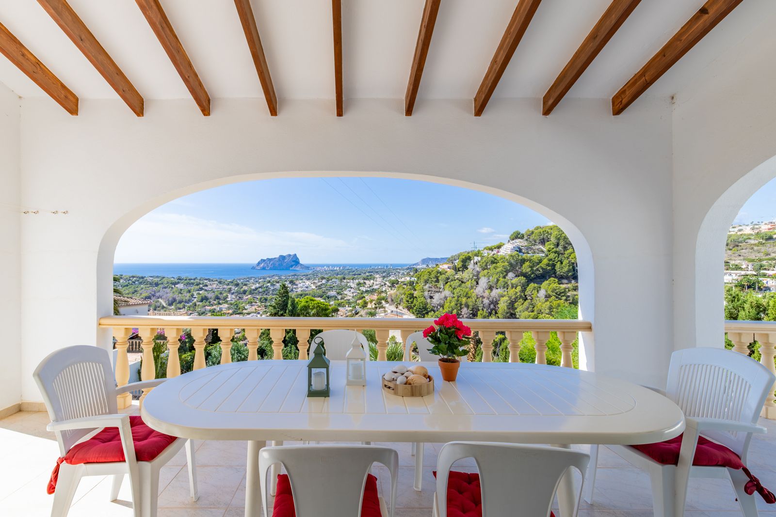 Overdekt terras met houten balken en mediterrane bogen, met panoramisch uitzicht op de Middellandse Zee en de Peñón de Ifach vanaf de eethoek.