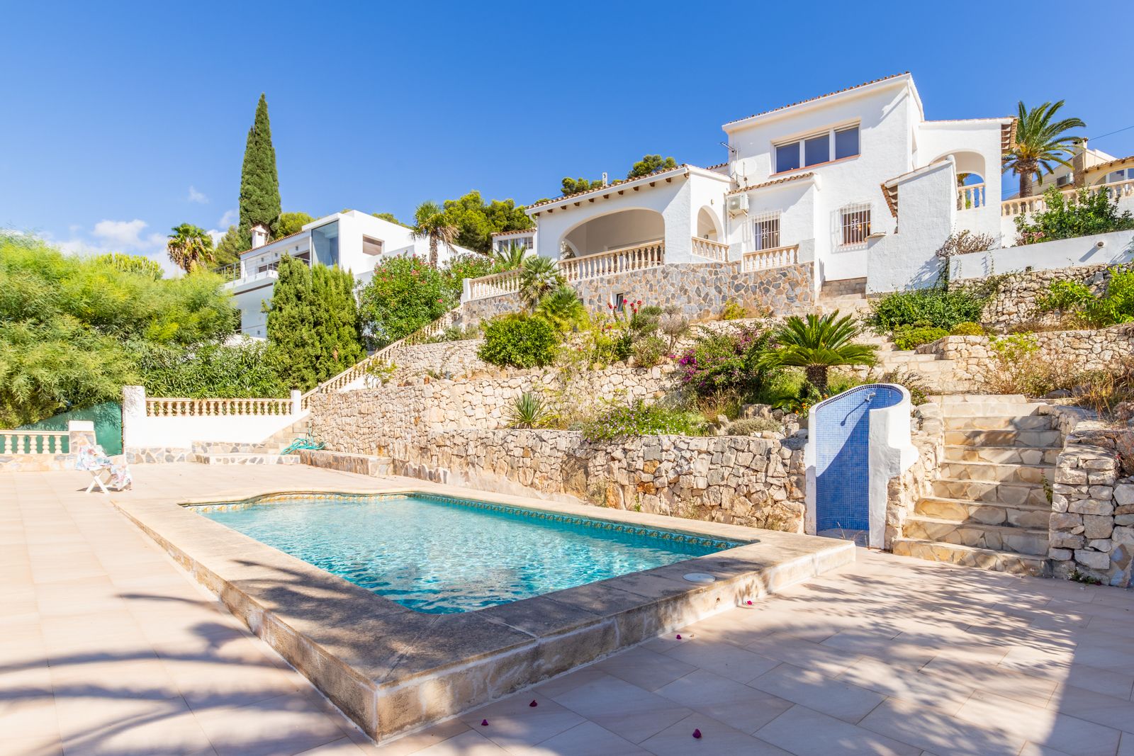 Privézwembad met stenen terras, omgeven door een trapsgewijze tuin met natuurstenen muren en een buitendouche bij deze mediterrane villa in Moraira.