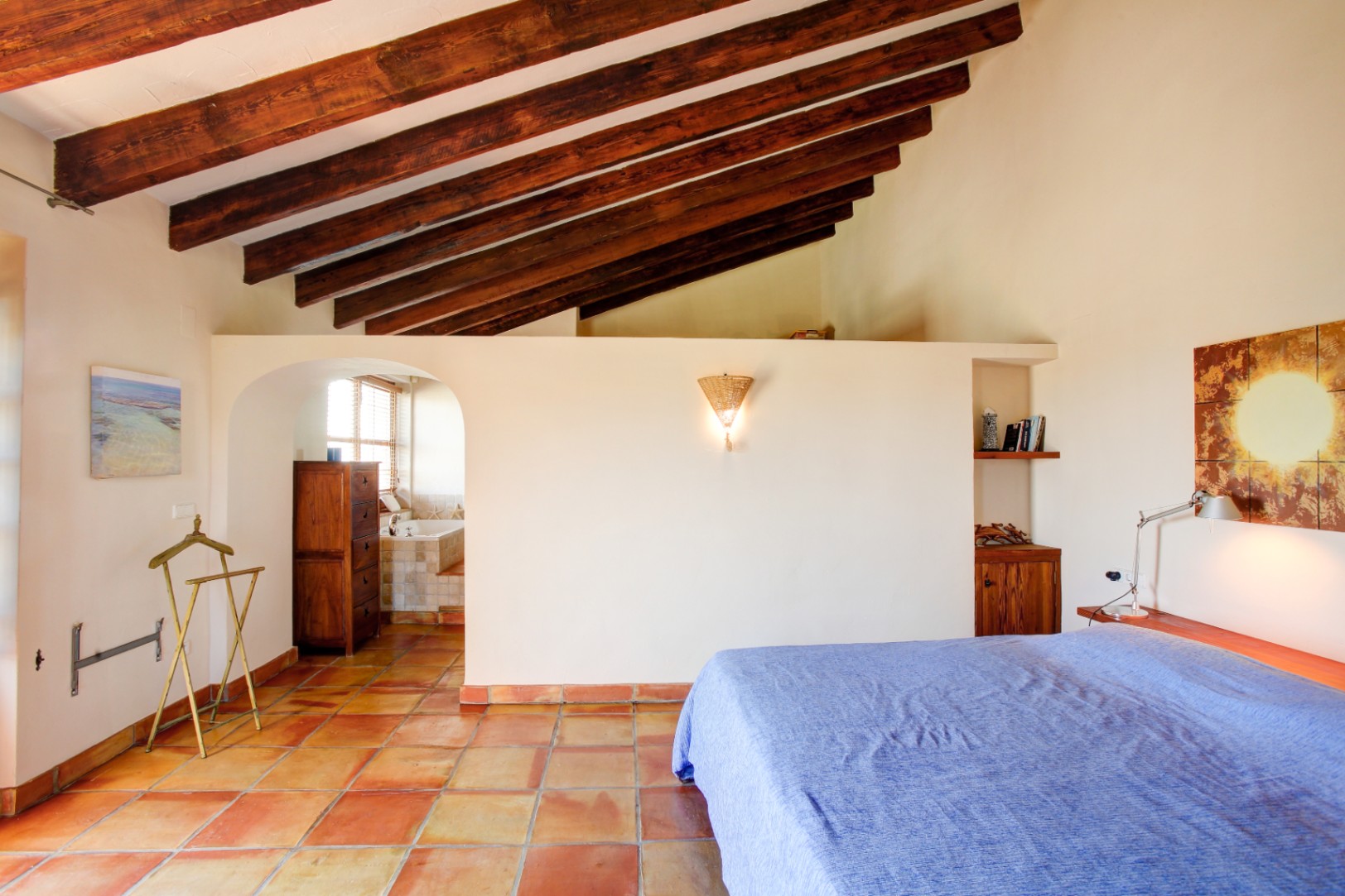 Hoofdslaapkamer met hoge plafonds voorzien van houten balken, een authentieke terracotta vloer en een boogdoorgang naar de aangrenzende badkamer.