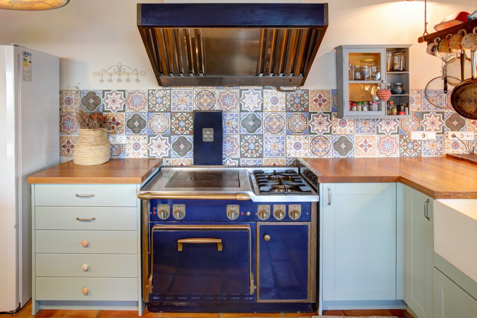 Professioneel blauw Molteni gasfornuis met koperen details, gecombineerd met een kleurrijke achterwand van patroontegels en massief houten werkbladen.