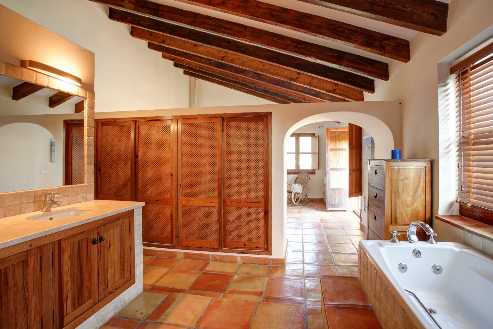 Rustieke badkamer met houten balkenplafond, terracotta vloer en hydromassagebad. Voorzien van houten inbouwkasten met vlechtwerk en een marmeren wastafelblad.