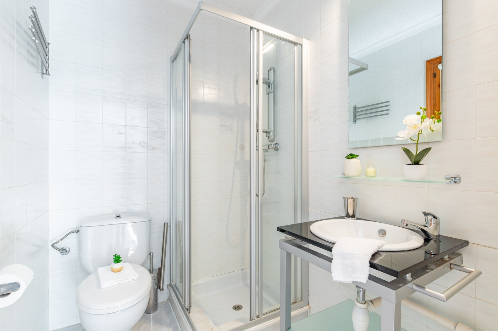 Badkamer met wit betegelde wanden, een glazen hoekdouchecabine en een wastafelmeubel voorzien van een donker stenen blad en ingebouwde wasbak.