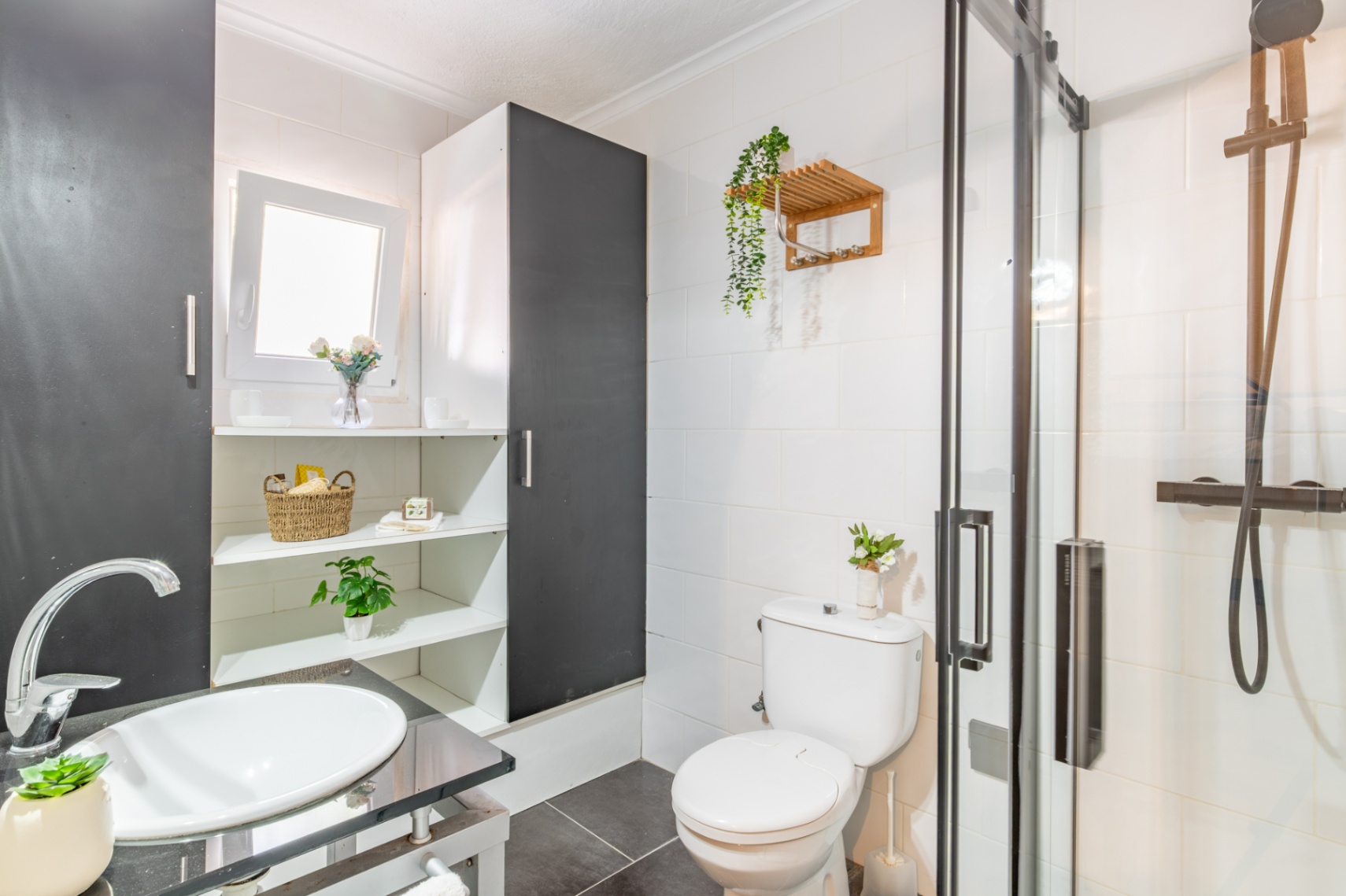 Functionele badkamer met glazen douchecabine, zwarte kranen en witte opzetwastafel. Voorzien van ingebouwde schappen en witte wandtegels.