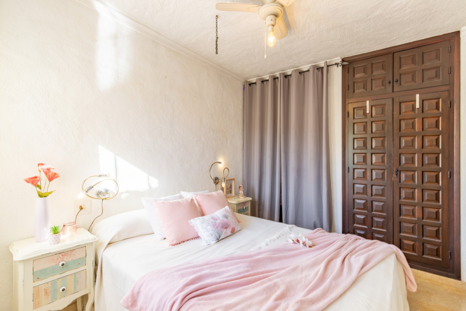 Slaapkamer met een ingebouwde donkerhouten kledingkast, witte muren met textuur en een plafondventilator. De ruimte geniet van veel natuurlijk lichtinval.