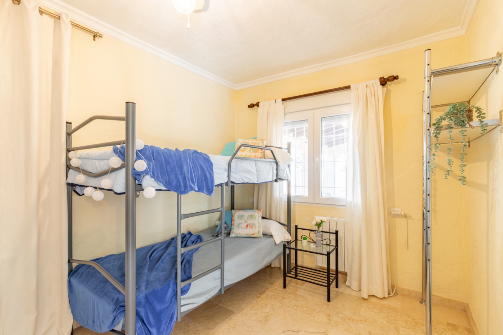 Slaapkamer met metalen stapelbed, crèmekleurige muren en een gepolijste natuurstenen vloer. Voorzien van een raam voor natuurlijk licht en open rekken.