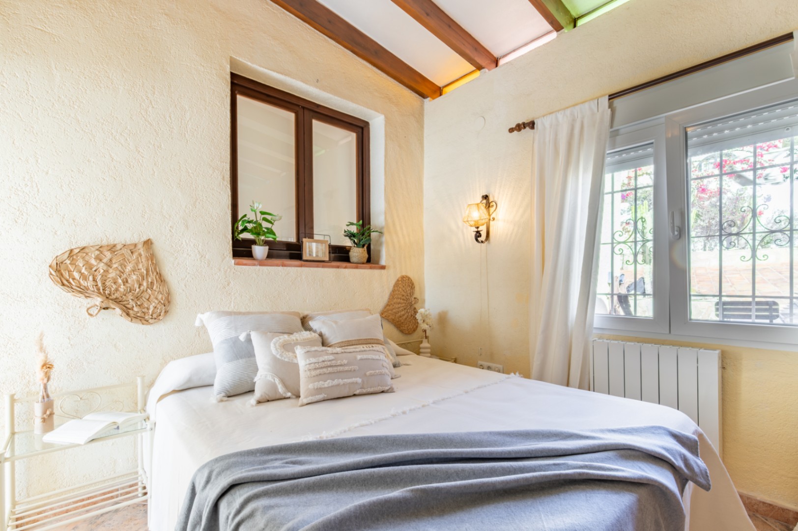 Slaapkamer met zichtbare houten plafondbalken, rustieke muren en twee ramen. De ruimte is ingericht met mediterrane accenten en een klassieke wandlamp.