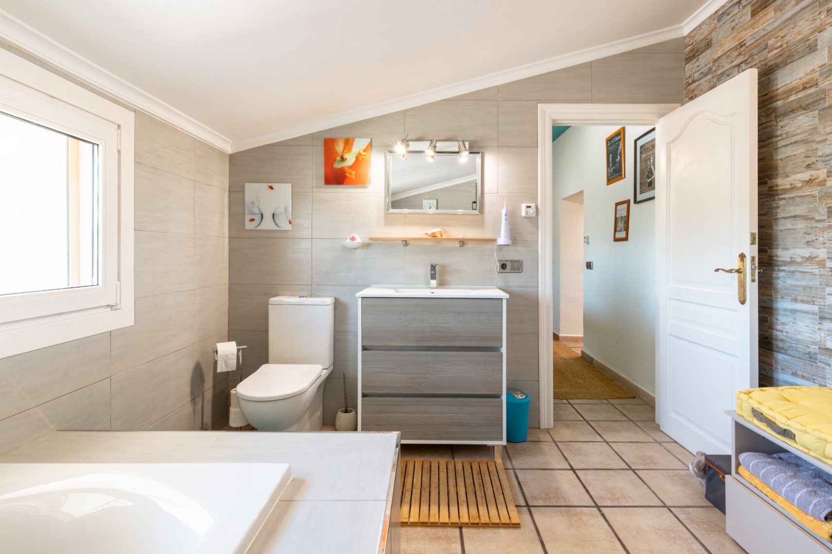 Gerenoveerde badkamer met schuin plafond, houten wastafelmeubel en grootformaat wandtegels, afgewerkt met een decoratieve stenen accentmuur.