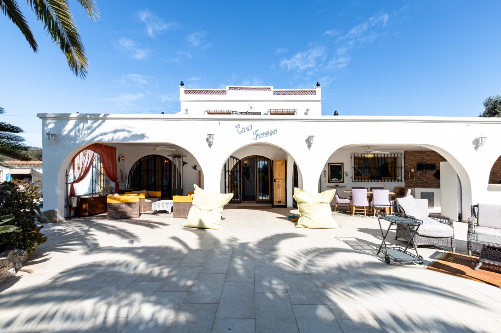 Mediterrane witte gevel met een naya met bogen, geplaveid terras en zithoeken buiten onder het bord "Casa Franziska".
