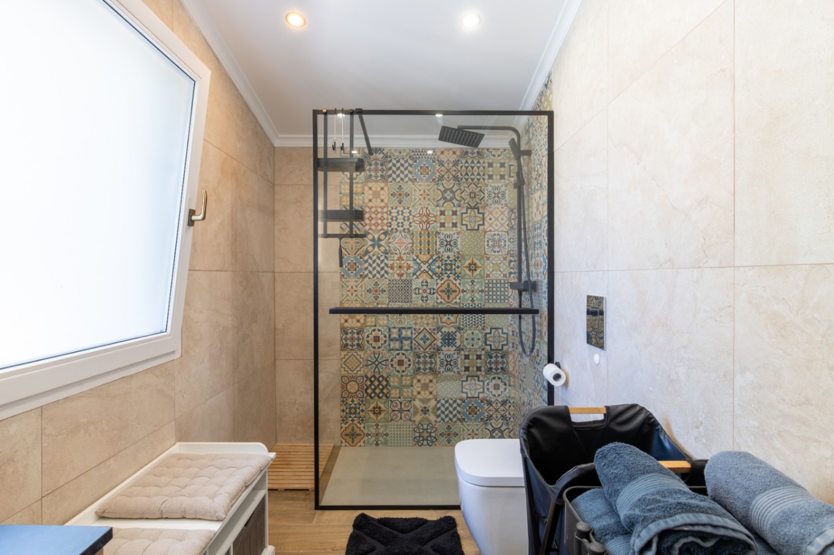 Moderne badkamer met inloopdouche, voorzien van decoratieve patroontegels, een zwart omrande glazen wand en een houtlook vloer.