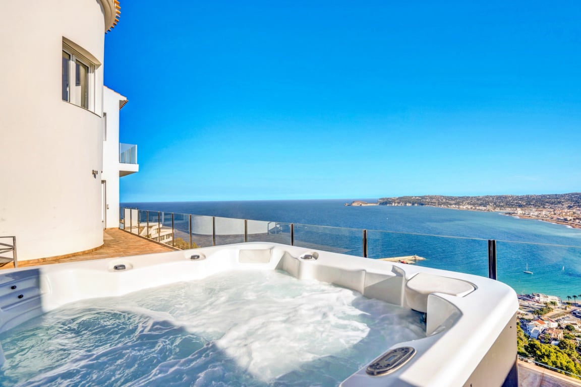 Buitenjacuzzi op een terras met glazen balustrade en panoramisch uitzicht over de Middellandse Zee en de haven van Jávea.