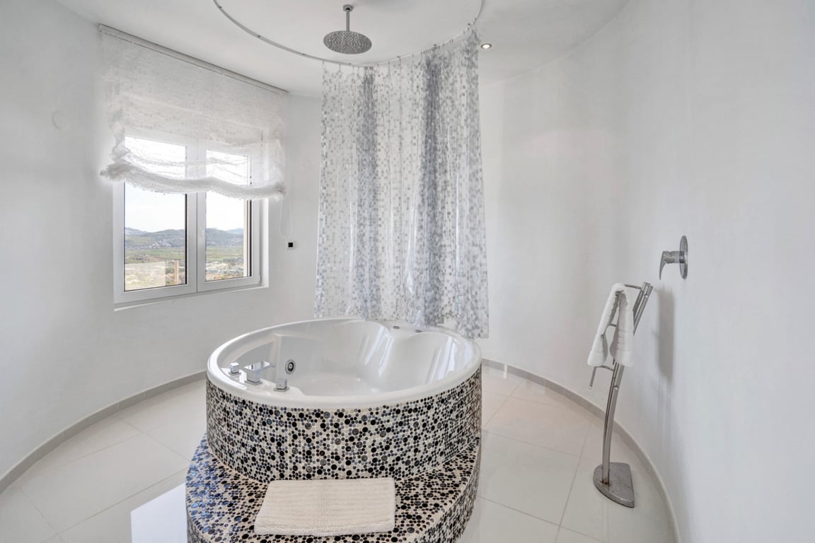 Designbadkamer met een rond hydromassagebad gedecoreerd met mozaïek, een geïntegreerde regendouche en een raam met uitzicht op de bergen.