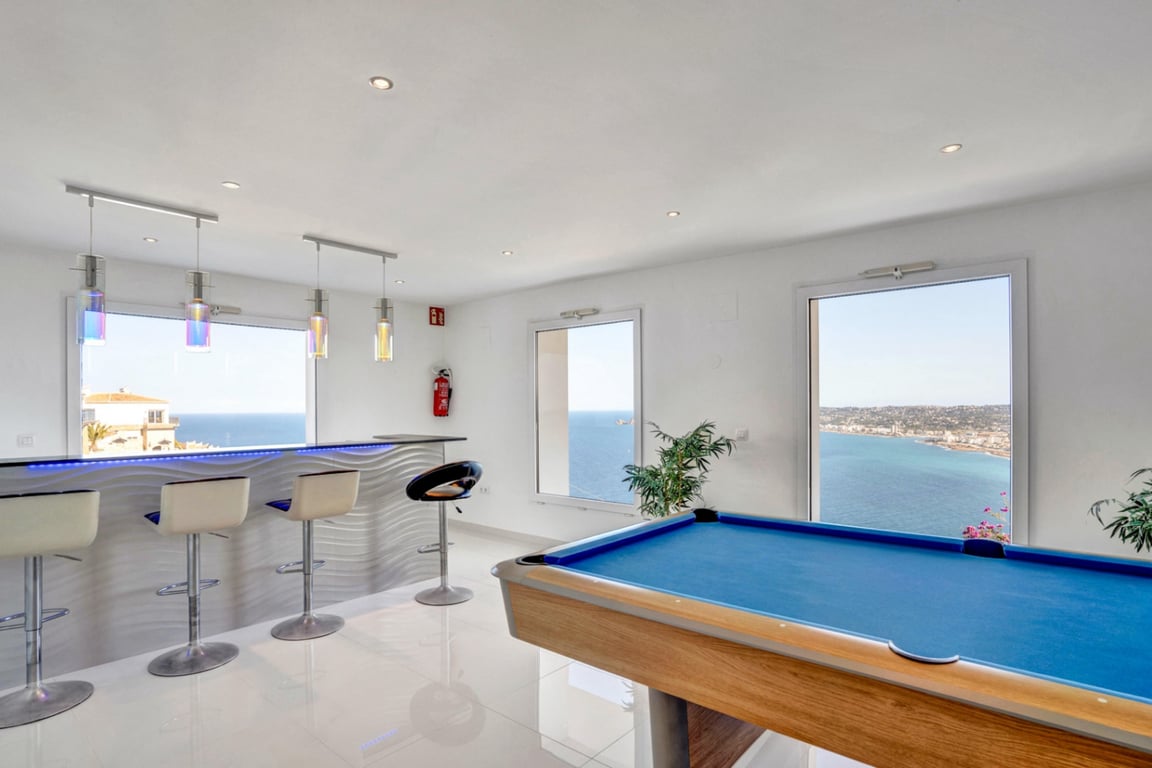 Entertainmentruimte met een blauwe biljarttafel en een moderne bar met LED-verlichting, met panoramisch uitzicht op zee door de grote ramen.