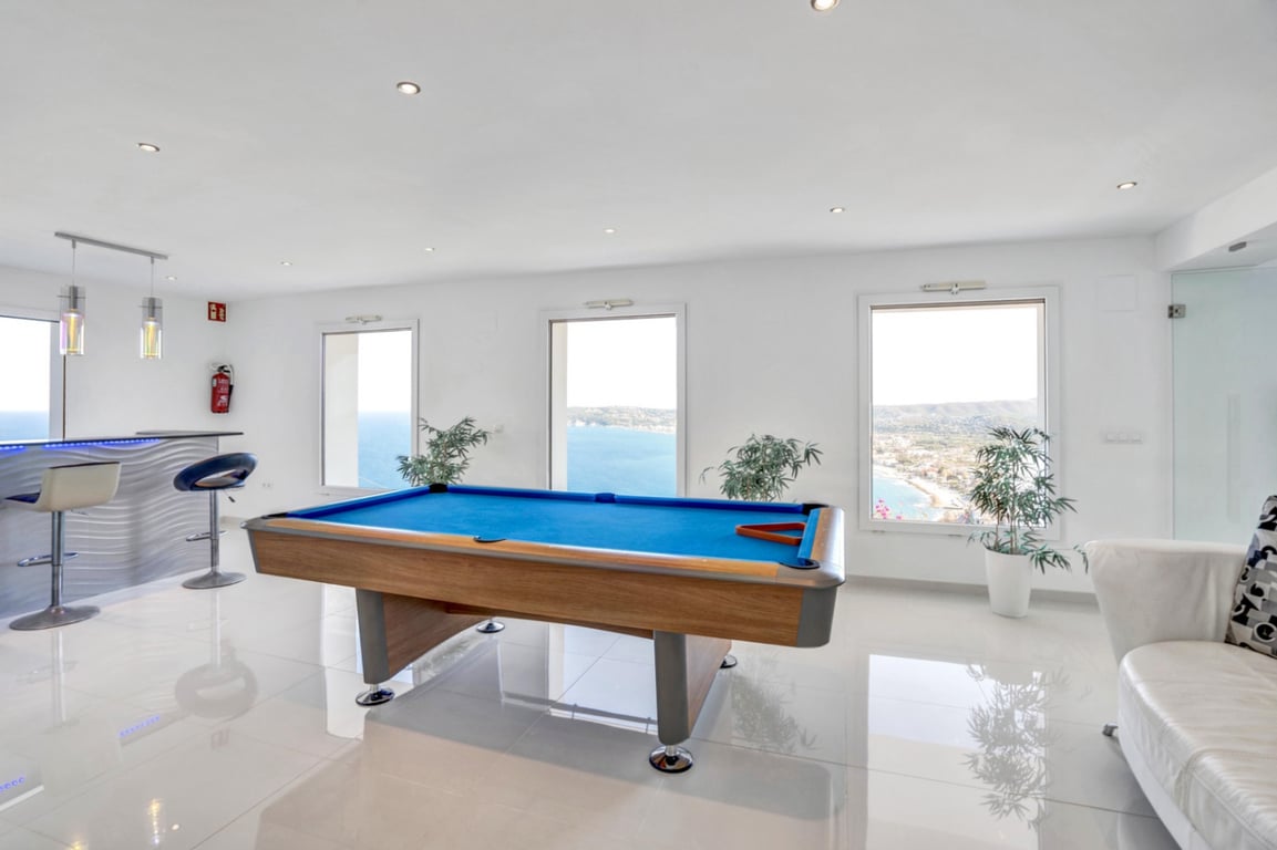 Gameroom met biljarttafel, bar en grote ramen met panoramisch uitzicht over de Middellandse Zee en de kustlijn van Jávea.