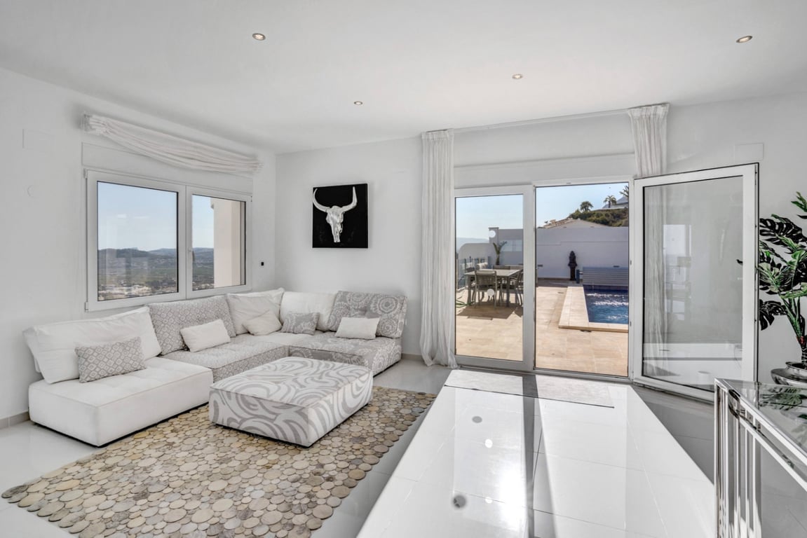 Lichte woonkamer met modulaire bank en directe toegang tot het terras met zwembad, met een panoramisch uitzicht over de zee en de bergen.