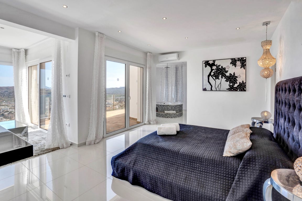 Master suite met gecapitonneerd hoofdbord, hoogglans tegelvloer en schuifpui naar het terras. Voorzien van een geïntegreerde mozaïek-jacuzzi met uitzicht op zee.