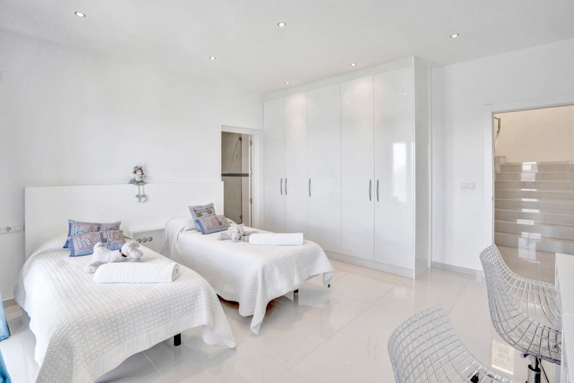 Minimalistische tweepersoonskamer met hoogglans inbouwkasten, gepolijste witte vloertegels en directe toegang tot de en-suite badkamer.